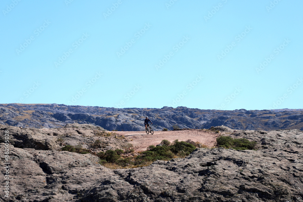 Man riding a bicycle in the mountain. Cyclists practicing mountain biking. Mountain bike. Mountains landscape. View of the Altas Cumbres, Córdoba, Argentina. Concept of travel, journey, adventure tour Man riding a bicycle in the mountain. Cyclists practicing mountain biking. Mountain bike. Mountains landscape. View of the Altas Cumbres, Córdoba, Argentina. Concept of travel, journey, adventure tour