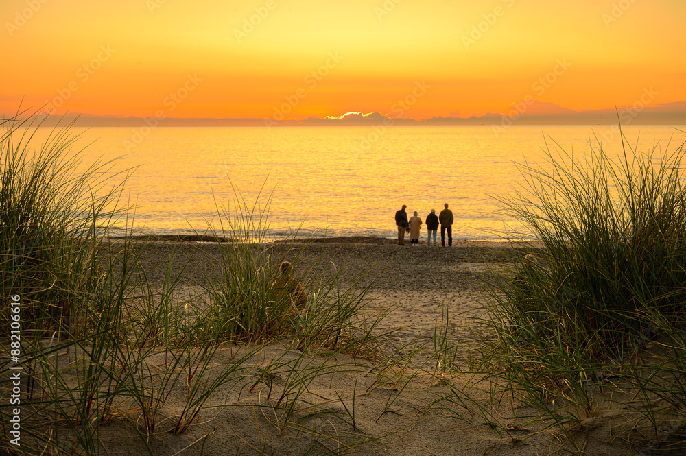 people sitting in the dunes watching the sunset in the sea