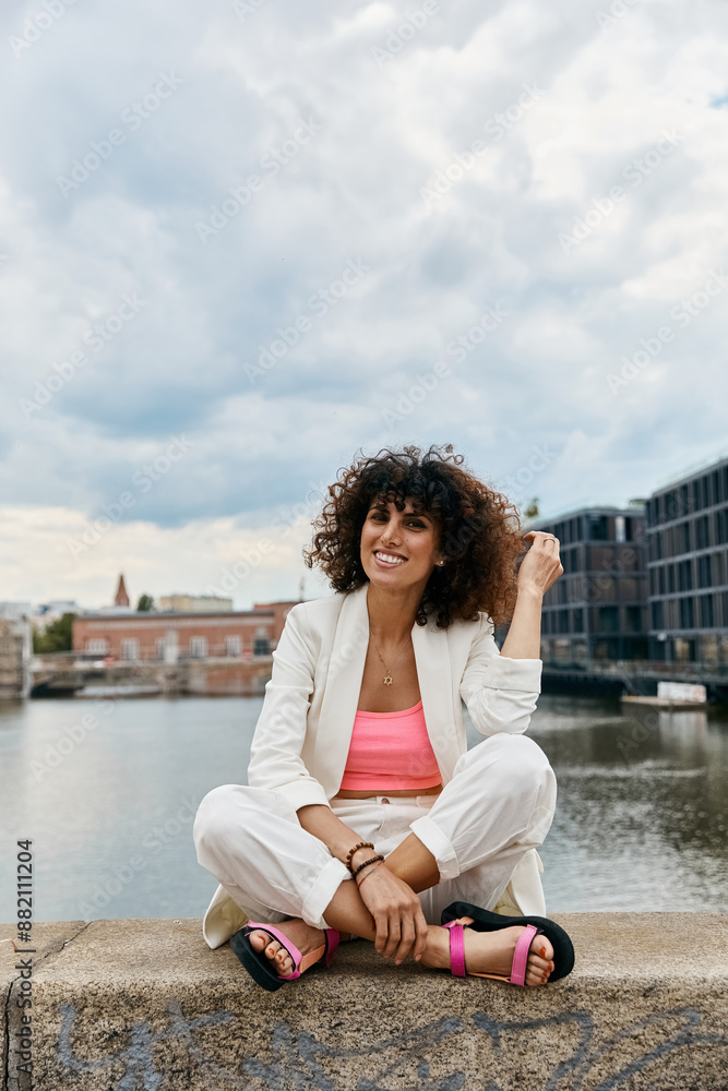 A woman in white clothing sits by the water in a European city, enjoying a sunny summer day. A woman in white clothing sits by the water in a European city, enjoying a sunny summer day.