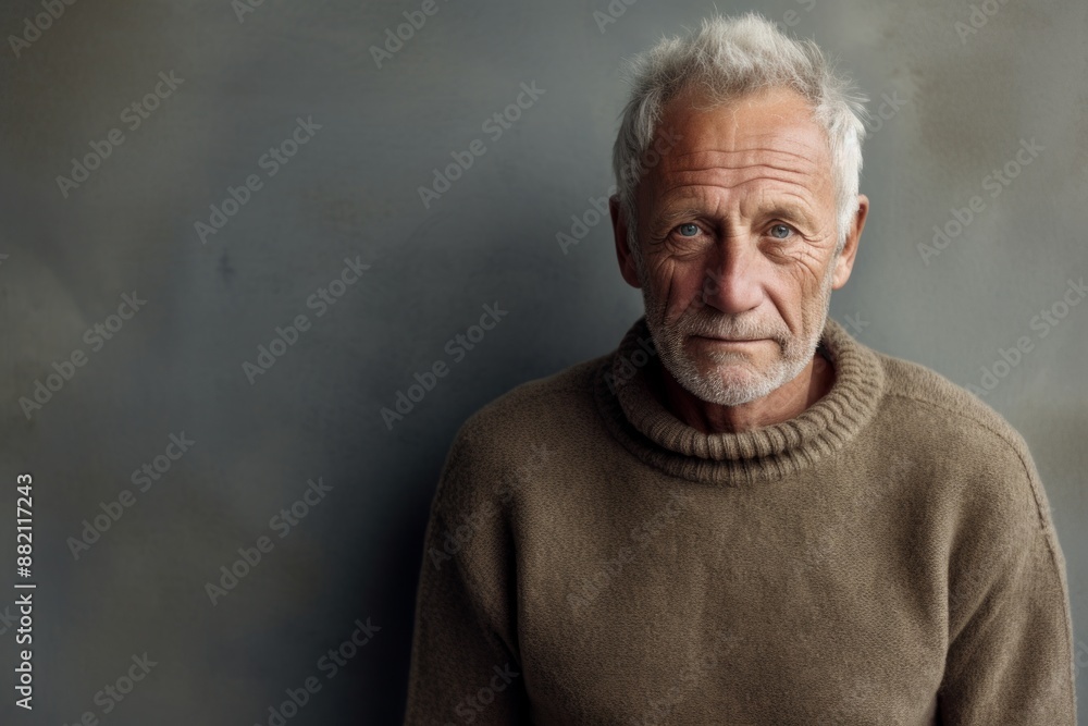 Portrait of a tender man in his 70s wearing a cozy sweater in bare concrete or plaster wall Portrait of a tender man in his 70s wearing a cozy sweater in bare concrete or plaster wall