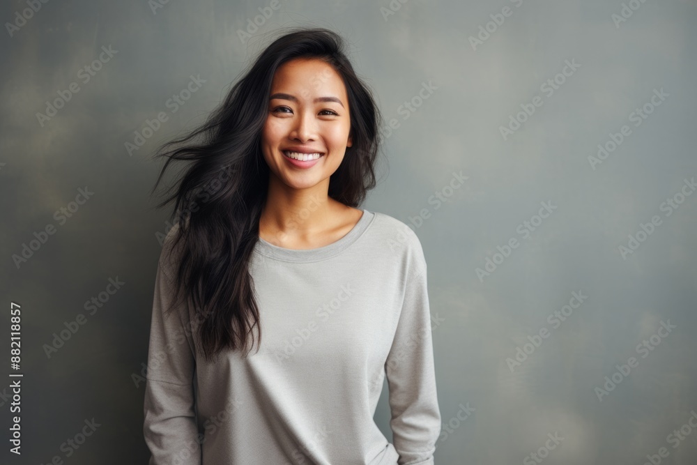 Portrait of a joyful asian woman in her 20s showing off a thermal merino wool top over bare concrete or plaster wall Portrait of a joyful asian woman in her 20s showing off a thermal merino wool top over bare concrete or plaster wall