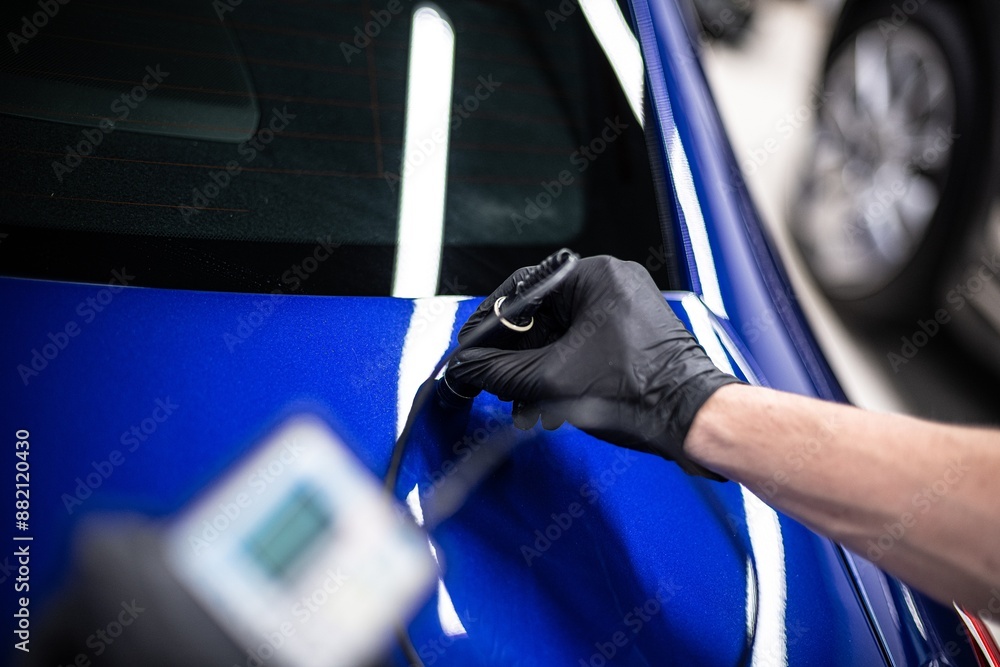 Image shows a person measuring the paint thickness on a blue car using a specialized device