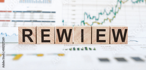 Fotografi Wooden blocks spelling the word review are placed on a table with blurred financial charts in the background