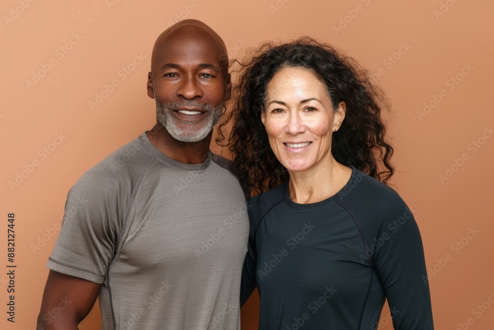 Portrait of a satisfied mixed race couple in their 40s wearing a moisture-wicking running shirt isolated in pastel brown background Portrait of a satisfied mixed race couple in their 40s wearing a moisture-wicking running shirt isolated in pastel brown background