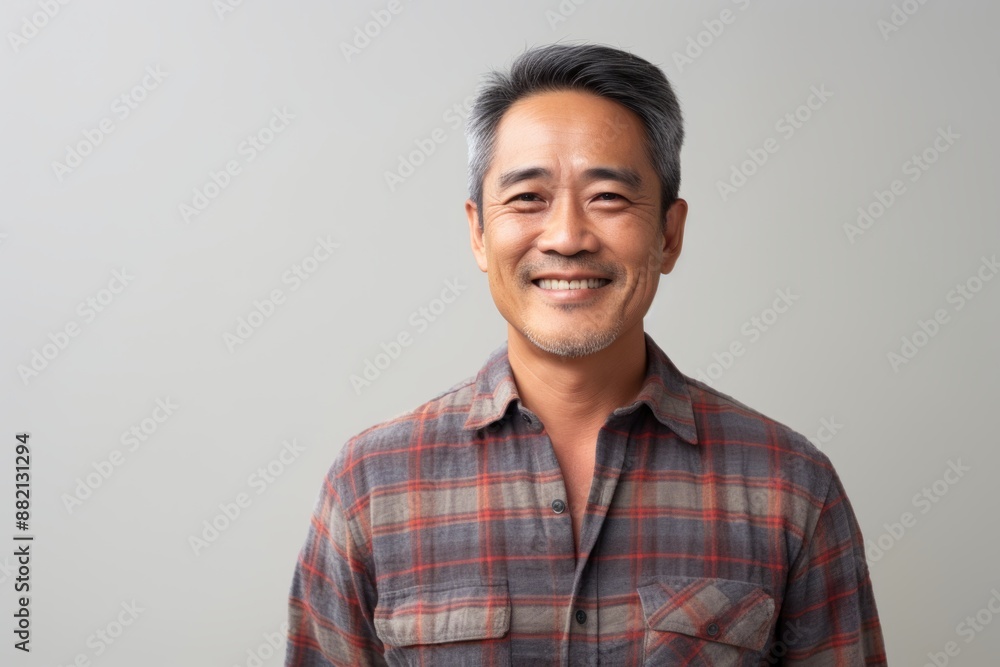 Portrait of a satisfied asian man in his 50s wearing a comfy flannel shirt isolated in light wood minimalistic setup Portrait of a satisfied asian man in his 50s wearing a comfy flannel shirt isolated in light wood minimalistic setup