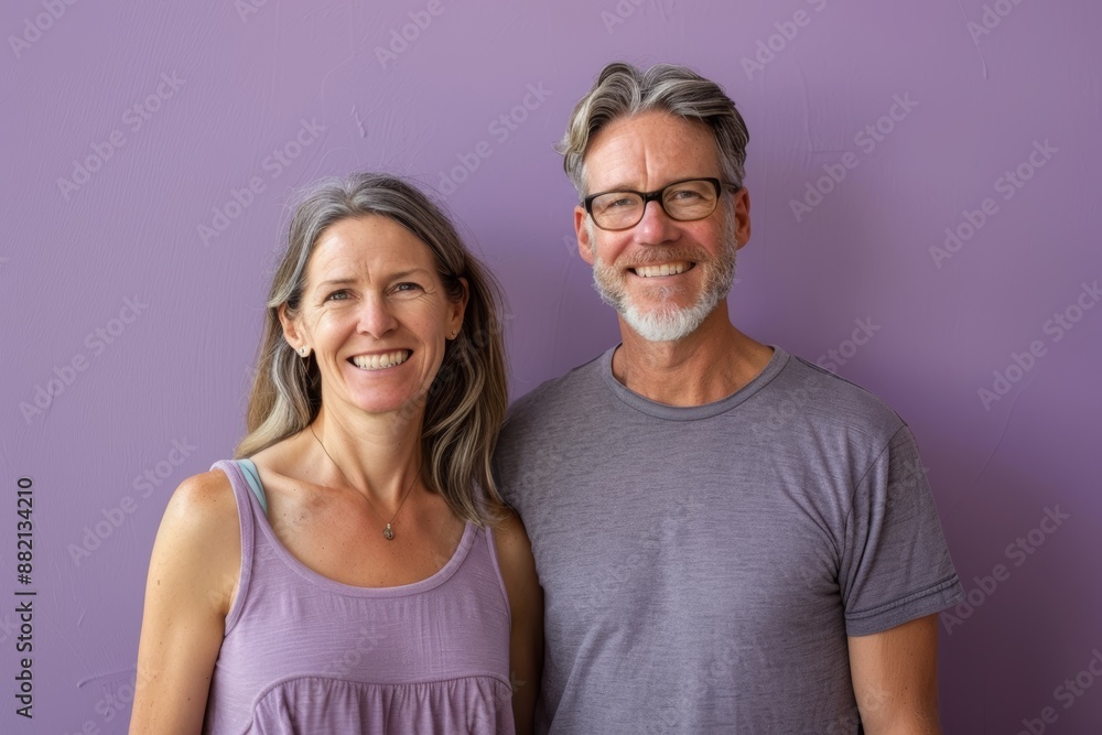 Portrait of a grinning couple in their 50s dressed in a casual t-shirt over soft purple background Portrait of a grinning couple in their 50s dressed in a casual t-shirt over soft purple background