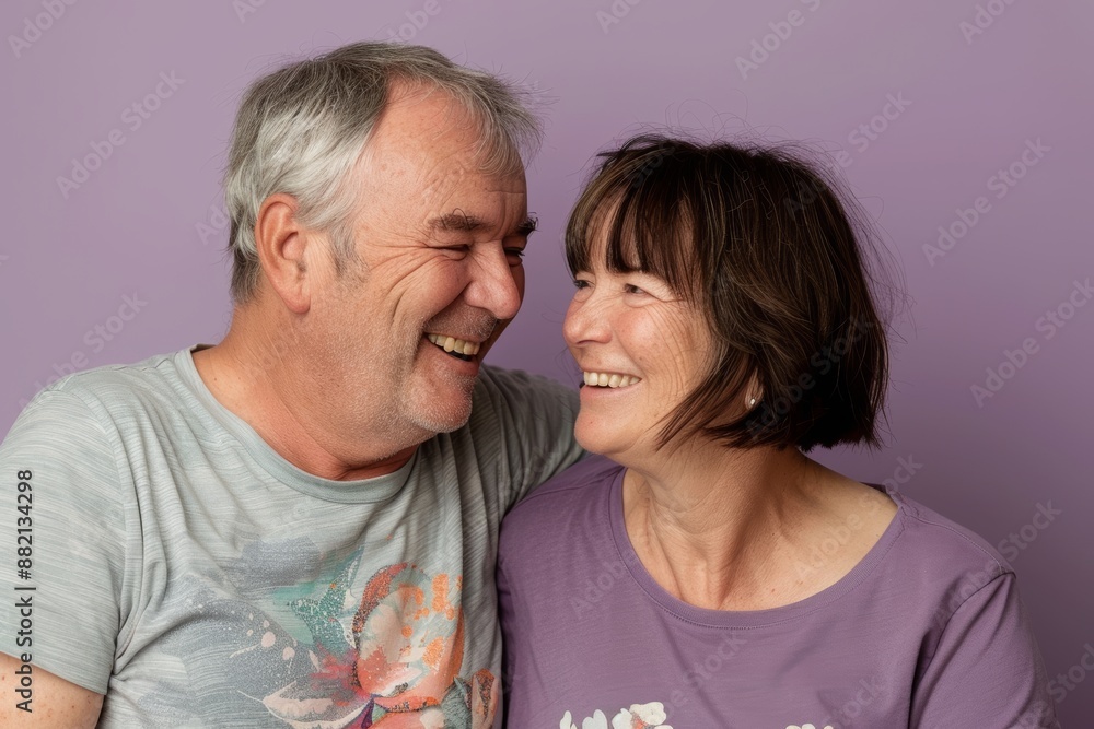 Portrait of a grinning couple in their 50s dressed in a casual t-shirt in front of soft purple background Portrait of a grinning couple in their 50s dressed in a casual t-shirt in front of soft purple background