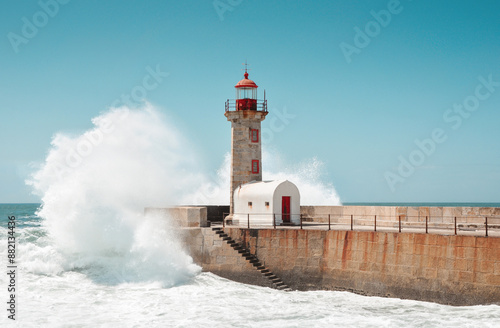 Wave crashing into lighthouse on the stone mole. The Felgueiras Lighthouse at Douro river mouth in Foz do Douro near Porto. Blue sky and Atlantic Ocean in the background. photo