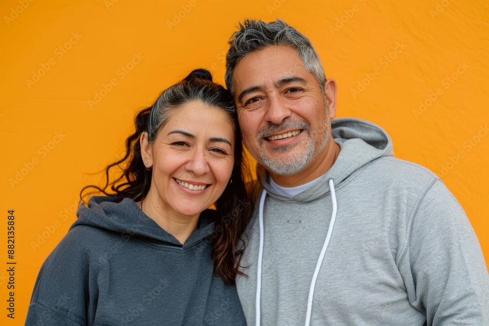 Portrait of a glad latino couple in their 40s sporting a comfortable hoodie in soft orange background Portrait of a glad latino couple in their 40s sporting a comfortable hoodie in soft orange background