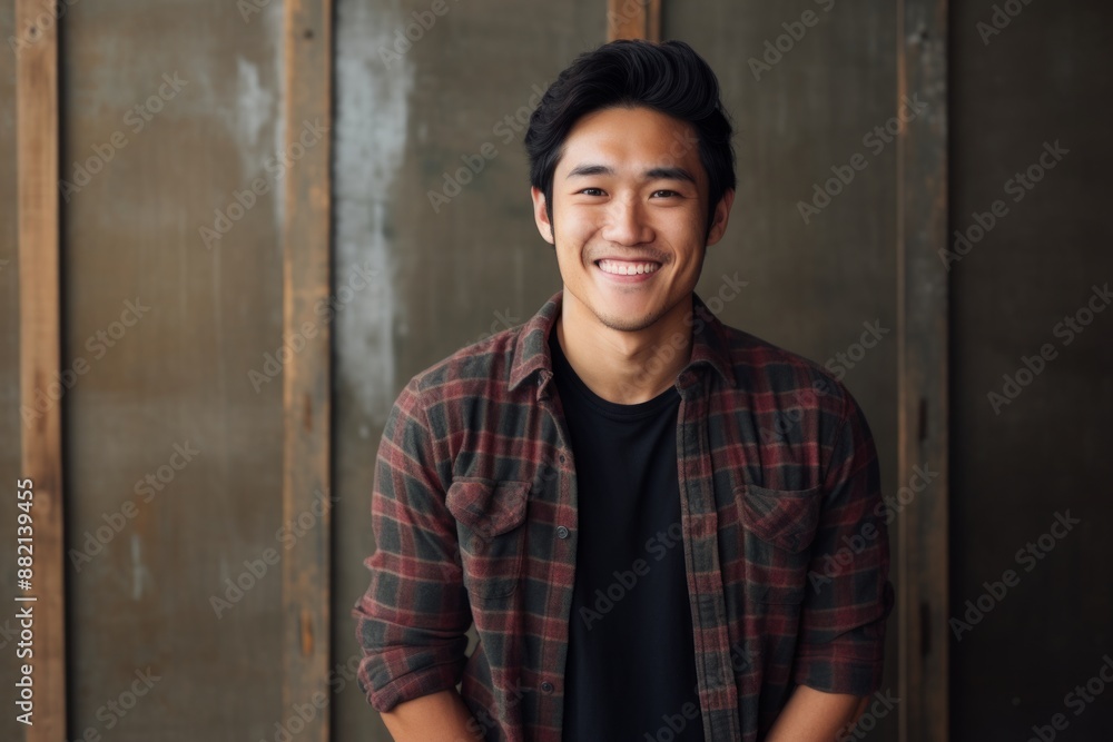Portrait of a smiling asian man in his 20s wearing a comfy flannel shirt in front of empty modern loft background Portrait of a smiling asian man in his 20s wearing a comfy flannel shirt in front of empty modern loft background