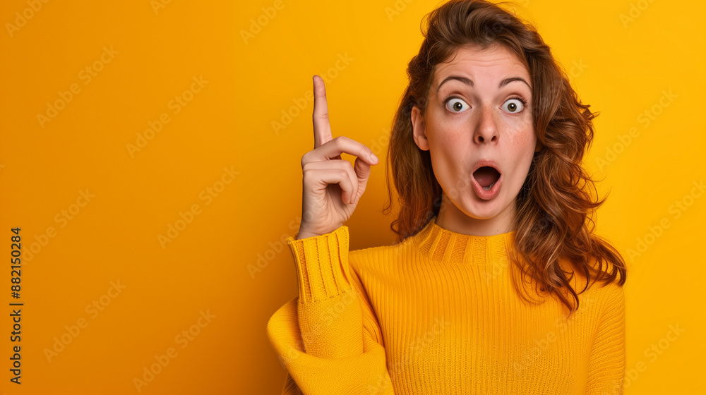 Surprised and shocked young beautiful woman pointing her finger up wearing yellow sweater on vibrant yellow background Surprised and shocked young beautiful woman pointing her finger up wearing yellow sweater on vibrant yellow background