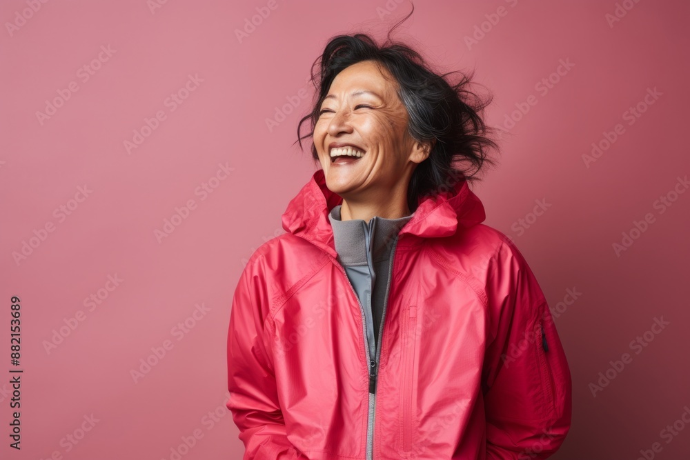 Portrait of a joyful asian woman in her 60s wearing a windproof softshell isolated on bare monochromatic room Portrait of a joyful asian woman in her 60s wearing a windproof softshell isolated on bare monochromatic room