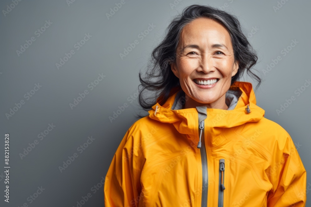 Portrait of a joyful asian woman in her 60s wearing a windproof softshell isolated on bare monochromatic room Portrait of a joyful asian woman in her 60s wearing a windproof softshell isolated on bare monochromatic room