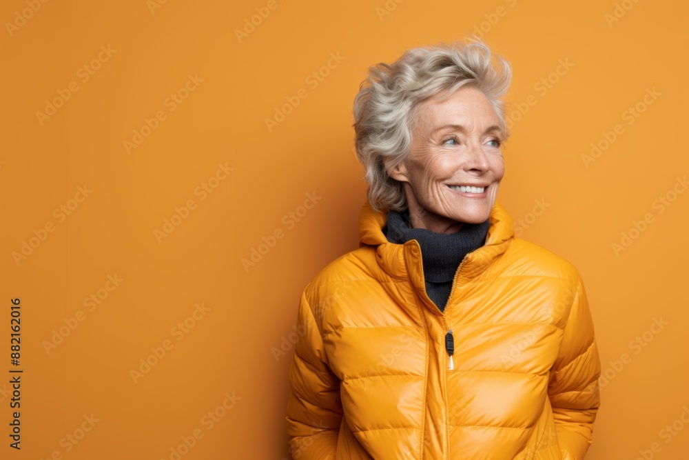 Portrait of a jovial woman in her 50s sporting a quilted insulated jacket on plain cyclorama studio wall Portrait of a jovial woman in her 50s sporting a quilted insulated jacket on plain cyclorama studio wall