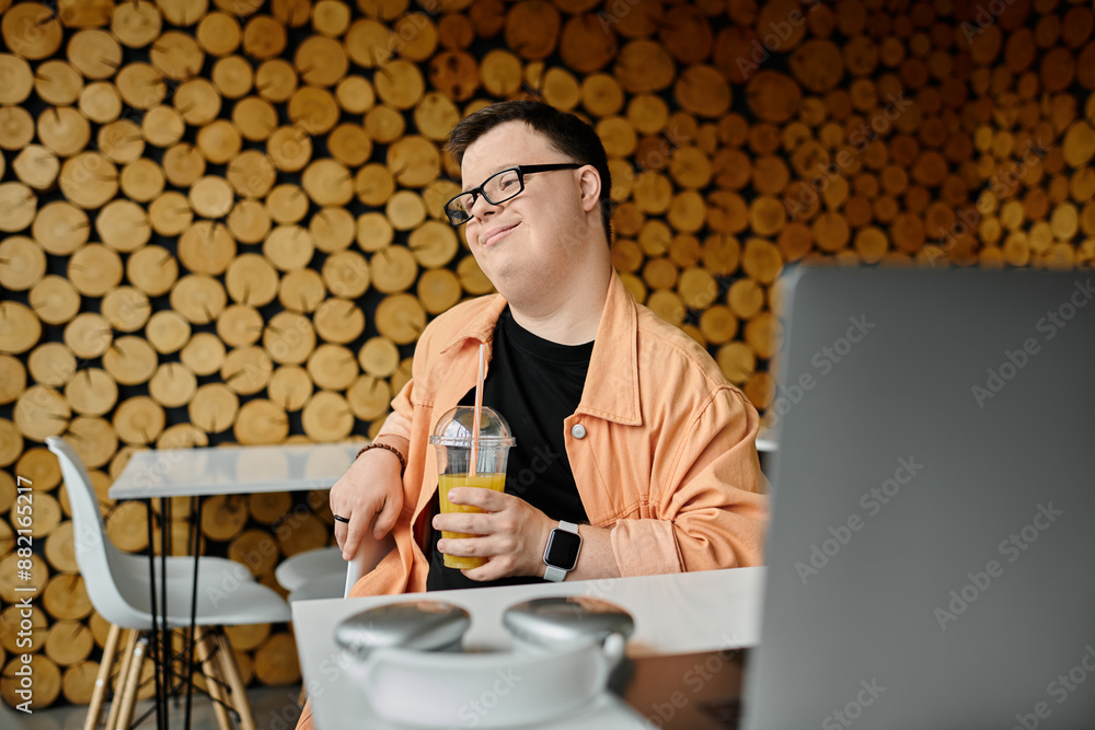 A man with Down syndrome enjoys a beverage while working on his laptop in a cafe. A man with Down syndrome enjoys a beverage while working on his laptop in a cafe.