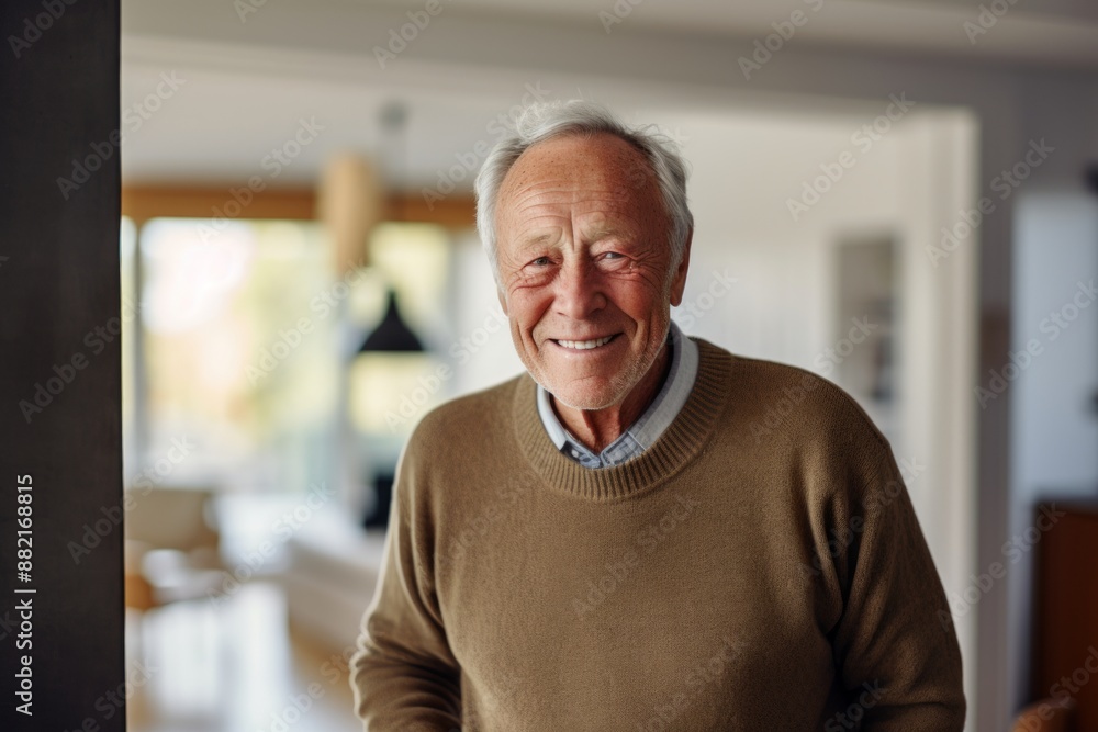 Portrait of a happy man in his 80s wearing a cozy sweater on crisp minimalistic living room Portrait of a happy man in his 80s wearing a cozy sweater on crisp minimalistic living room