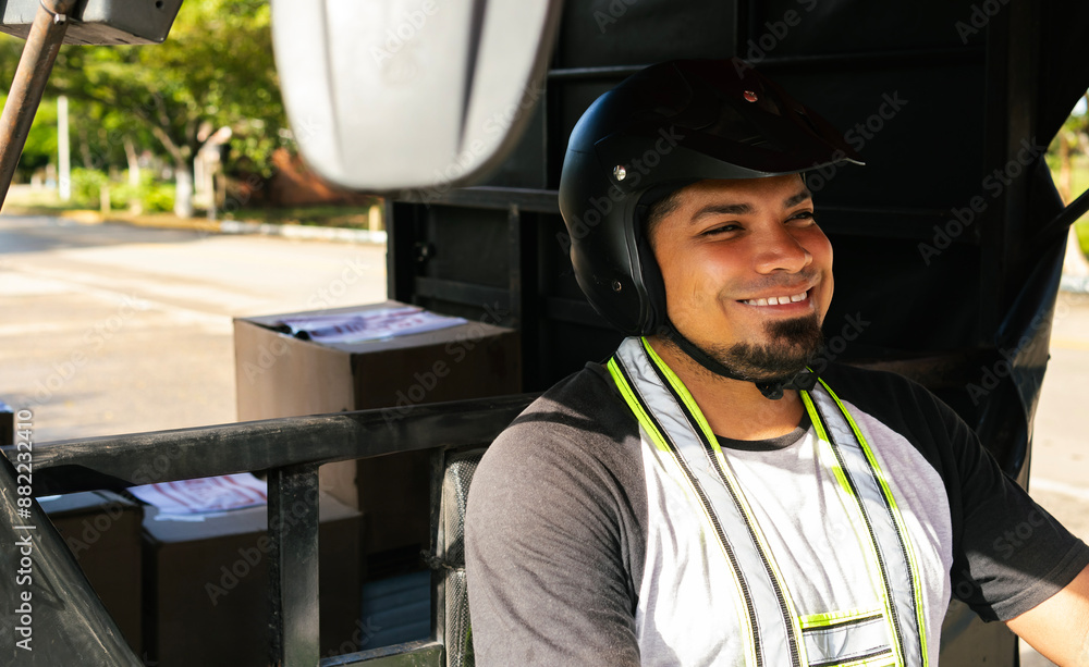 A Latin delivery worker in their 30s smiling while driving a three-wheeled vehicle, wearing a helmet and vest, carrying packages or boxes in the vehicle's cargo area A Latin delivery worker in their 30s smiling while driving a three-wheeled vehicle, wearing a helmet and vest, carrying packages or boxes in the vehicle's cargo area