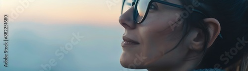 Close-up side profile of a woman wearing glasses, gazing thoughtfully into the distance at sunset.