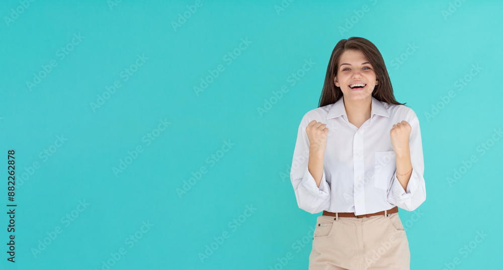 Portrait of young woman 20s wearing white shirt clenching fist like rejoicing victory or triumph isolated over blue background Portrait of young woman 20s wearing white shirt clenching fist like rejoicing victory or triumph isolated over blue background