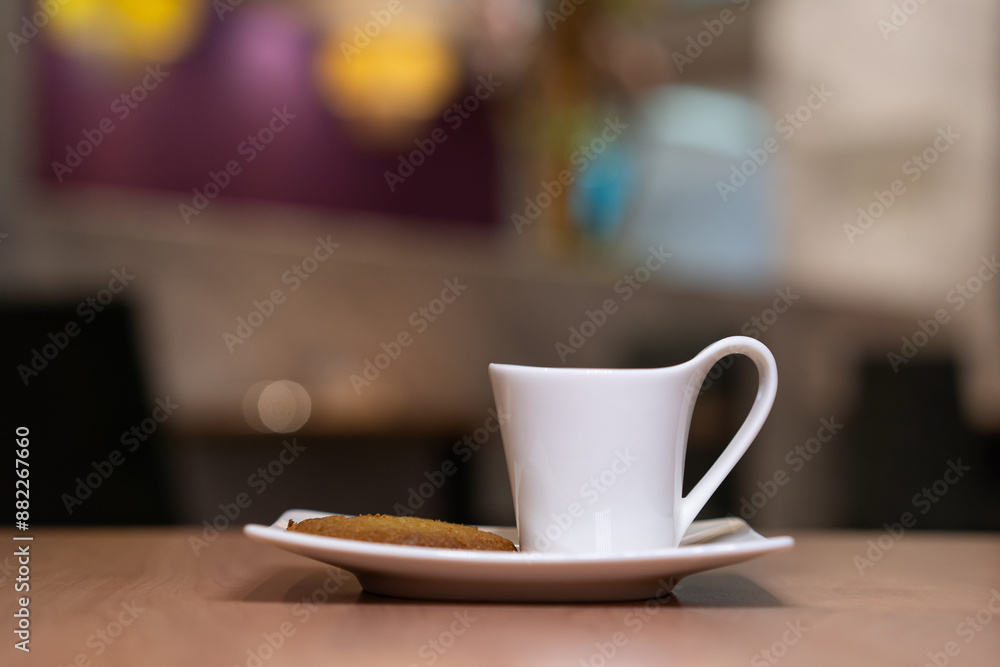 White cup filled with coffee on a plate with biscuit on beside. White cup filled with coffee on a plate with biscuit on beside.