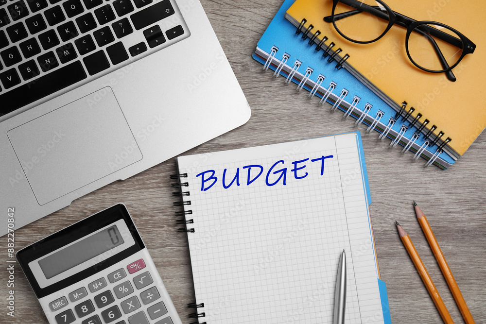 Notebook with word Budget, calculator, glasses and laptop on wooden table, flat lay Notebook with word Budget, calculator, glasses and laptop on wooden table, flat lay
