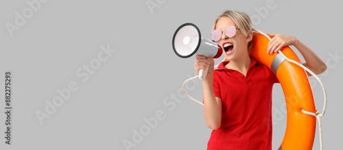 фотографія Little lifeguard holding lifebuoy and megaphone on grey background with space fo