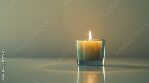 In a small, quiet interior, a single candle burning in a small glass container throws its light onto a simple, single-color wall.