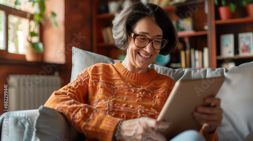 Happy pretty elder woman using digital tablet computer at home, reading electronic book, talking on video call, enjoying online communication, domestic Internet technology