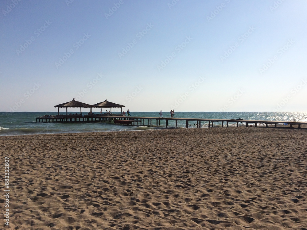 Fototapeta premium A wide pier on the beach leads to two gazebos or bungalows in the sea