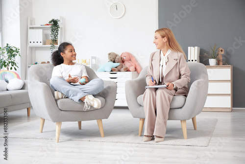 African-American girl with ball talking to psychologist in armchairs at office