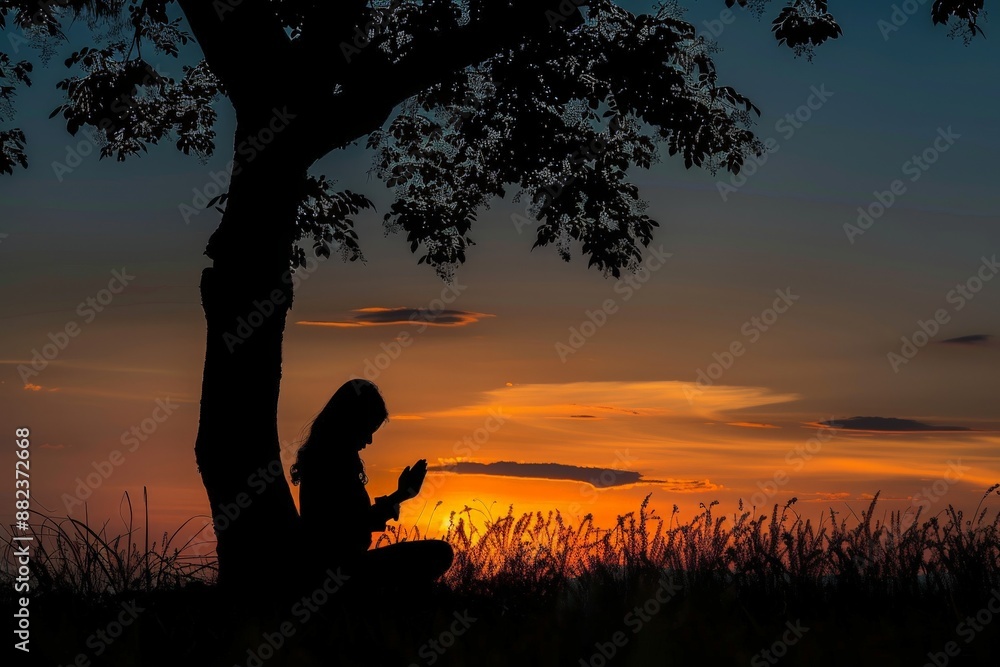 Silhouette of a woman kneeling praying under a tree at sunset Silhouette of a woman kneeling praying under a tree at sunset