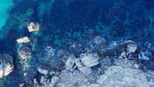 Tat-Tonn or Spritzing rock, snorkeling point between Qarraba Bay and Ta'Babu Cove, Ghajn Tuffieha, Mgar, Malta. Aerial view of the emerald sea and rocky coast in early morning still in the shade of photo