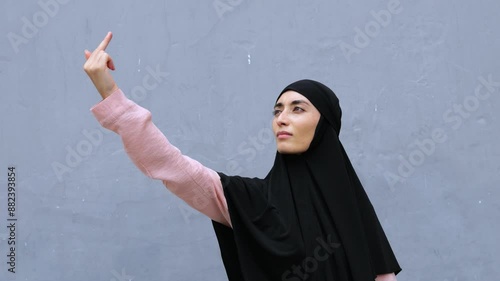 Muslim woman in hijab shows protest gesture middle finger. Gesture expresses strong emotions and disagreement. Traditional image and provocative gesture attracts attention, challenging stereotypes. photo