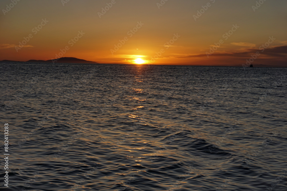Smooth sunset above purplish wavy sea surface with sun flares on it Smooth sunset above purplish wavy sea surface with sun flares on it
