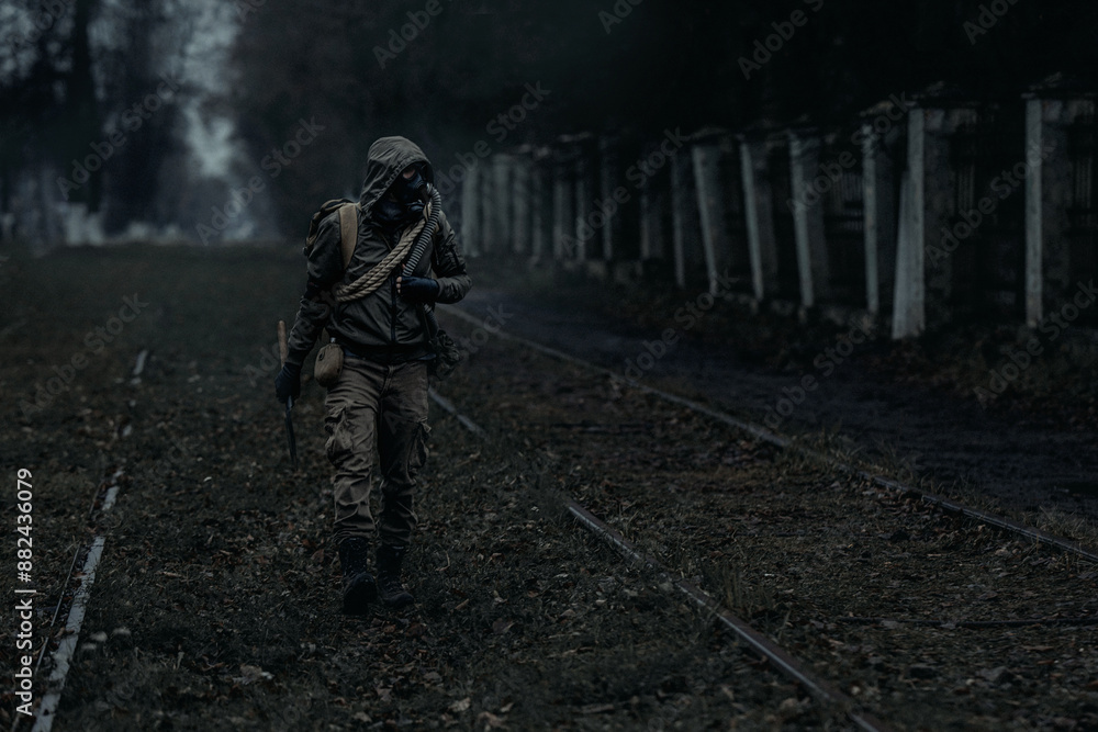 A man in a gas mask and camouflage walks through an abandoned, post-apocalyptic city. The concept of survival after a nuclear disaster and war.