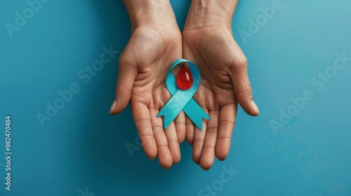 Wallpaper Mural A close-up image depicting a pair of hands carefully holding a teal awareness ribbon with a red droplet atop, symbolizing a cause or awareness campaign. Torontodigital.ca
