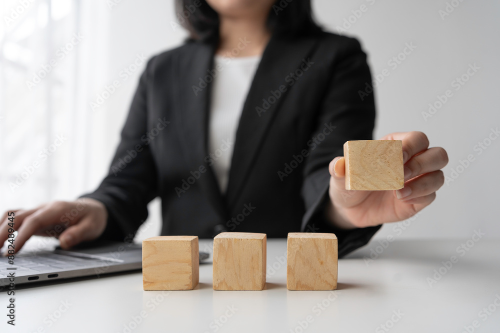 Businesswoman is completing a sequence of four wooden blocks on a desk, symbolizing a strategic approach to business development and growth Businesswoman is completing a sequence of four wooden blocks on a desk, symbolizing a strategic approach to business development and growth