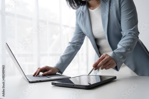 Focused businesswoman in a modern office, using laptop and tablet with stylus pen, showcasing professionalism and innovation photo