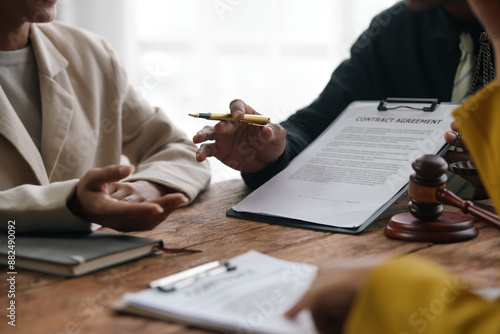 Lawyer is explaining a contract agreement to a client, pointing with a pen at specific clauses while sitting at a desk with a gavel