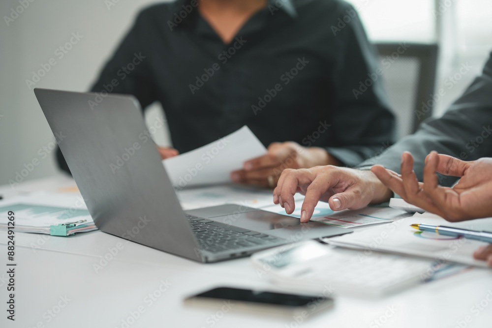 Busy professionals collaborate on a laptop, analyzing financial data with focus and determination in a modern office setting Busy professionals collaborate on a laptop, analyzing financial data with focus and determination in a modern office setting