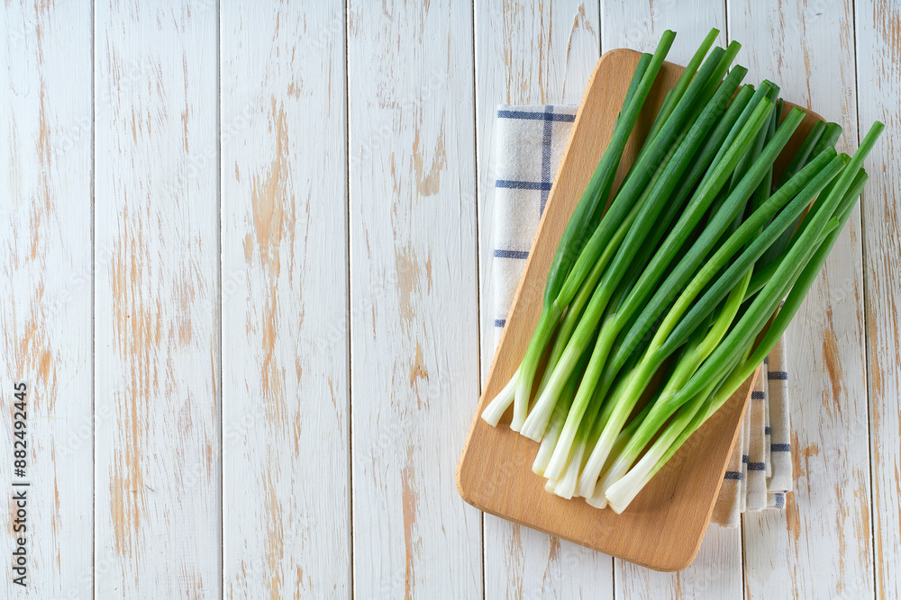 Fresh spring onions or scallions on a cutting board on white wooden table, top view. Fresh spring onions or scallions on a cutting board on white wooden table, top view.