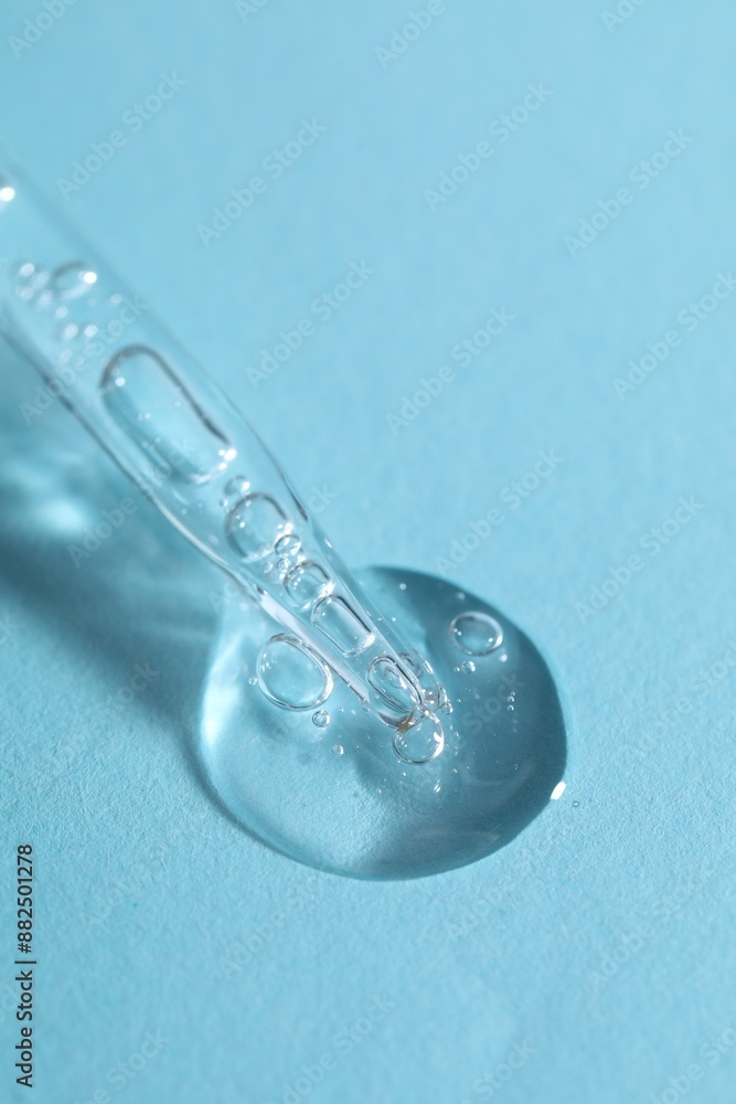 Glass pipette and transparent liquid on light blue background, closeup Glass pipette and transparent liquid on light blue background, closeup