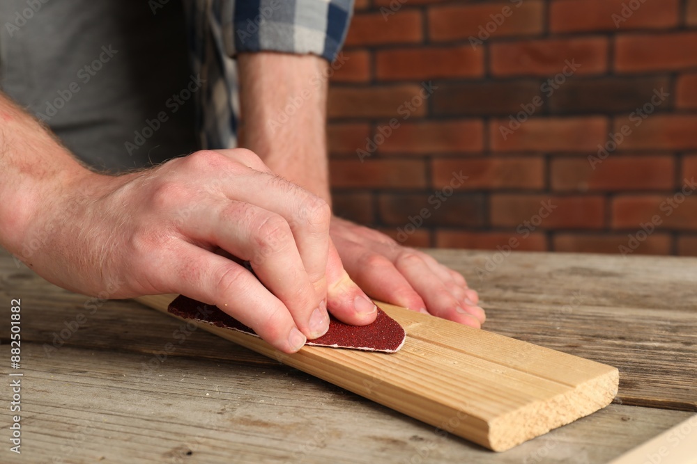 Man polishing wooden plank with sandpaper at table, closeup Man polishing wooden plank with sandpaper at table, closeup