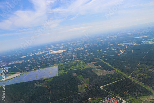 Aerial View of Expansive Solar Farm Amidst Verdant Forest and Urban Outskirts Under Clear Blue Sky