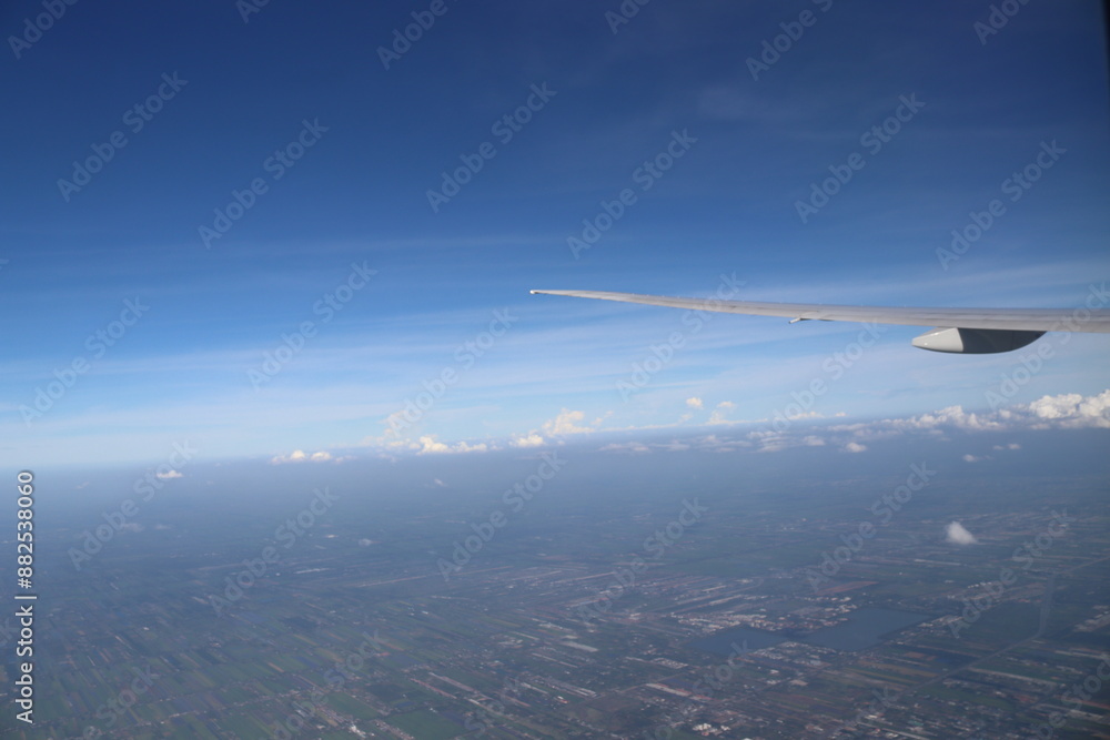 Aerial View of Urban Landscape with Airplane Wing Under Clear Blue Sky and Scattered Clouds Aerial View of Urban Landscape with Airplane Wing Under Clear Blue Sky and Scattered Clouds