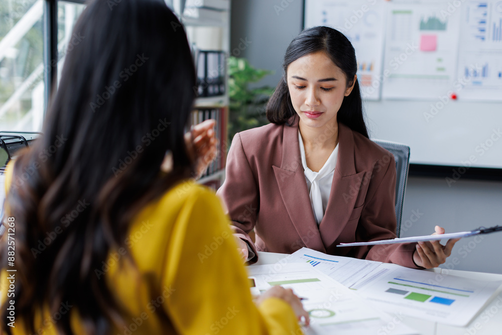 Obraz premium Two cheerful asian office workers women cooperating on project, sitting at desk with laptop using calculator, finance accounting analytical concept.