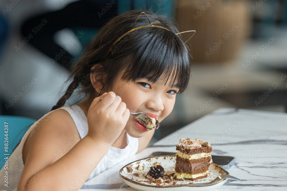 A six-year-old Malaysian girl eating a chocolate cake at a stylish cafe in Selangor, Malaysia, on an early summer afternoon. A six-year-old Malaysian girl eating a chocolate cake at a stylish cafe in Selangor, Malaysia, on an early summer afternoon.