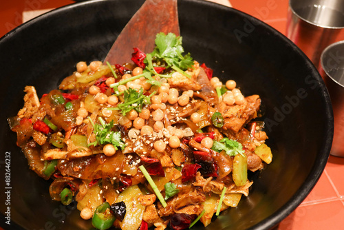 close up of Sichuan style spicy dry pot with peanut, beef tongue, beef stomach, celtuce, meat and noodles in a black bowl