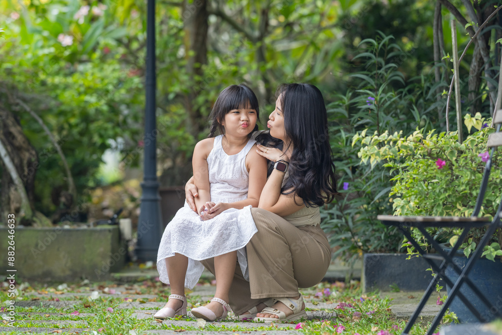A twenty-something Chinese Malaysian woman and a six-year-old girl spending time together among the greenery and flowers at a stylish cafe in Selangor, Malaysia, on a sunny early summer afternoon. A twenty-something Chinese Malaysian woman and a six-year-old girl spending time together among the greenery and flowers at a stylish cafe in Selangor, Malaysia, on a sunny early summer afternoon.