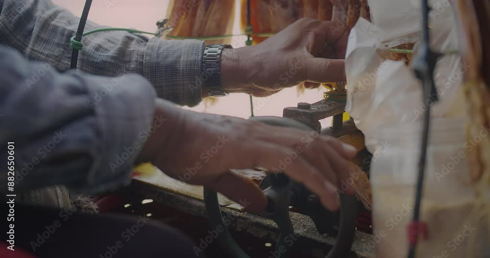 Close-up of a street vendor's hands using a manual machine to prepare dried squid being crushed into sheets in an outdoor market setting. Close-up of a street vendor's hands using a manual machine to prepare dried squid being crushed into sheets in an outdoor market setting.